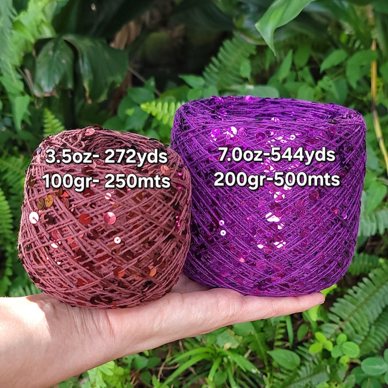 May include: Two balls of yarn with sequins, one in a deep maroon and one in a vibrant purple. The maroon ball is labeled 3.5oz- 272yds and 100gr- 250mts. The purple ball is labeled 7.0oz- 544yds and 200gr- 500mts. Both are textured with shiny discs.