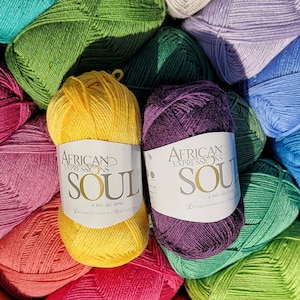 May include: A close-up of colorful yarn skeins. Two skeins are in focus, one yellow and one purple, each with a label that reads "AFRICAN EXPRESSIONS SOUL". The text "-it feels like home- Lovingly Blended for a Silky Soft Touch" is also visible.
