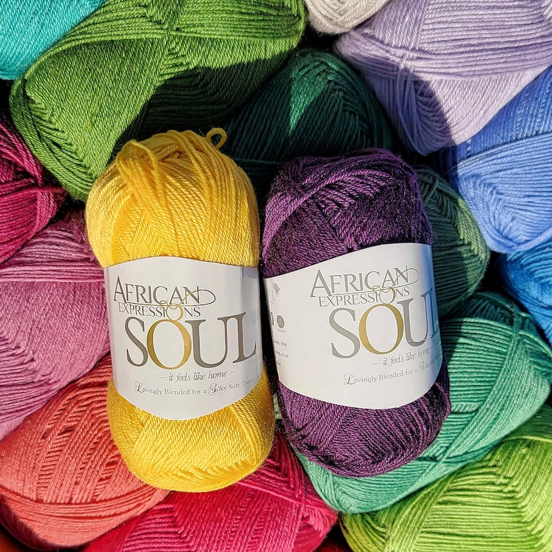 May include: A close-up of colorful yarn skeins. Two skeins are in focus, one yellow and one purple, each with a label that reads "AFRICAN EXPRESSIONS SOUL". The text "-it feels like home- Lovingly Blended for a Silky Soft Touch" is also visible.