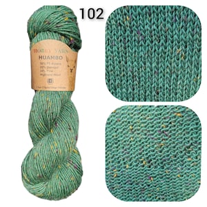 May include: A skein of green Hobby Yarn Huambo wool blend with flecks of yellow and purple. The label reads "50% FS Alpaca, 20% Donegal, 30% Fine Highland Wool". The number "102" is printed in white. Two close-up knit swatches are also shown.