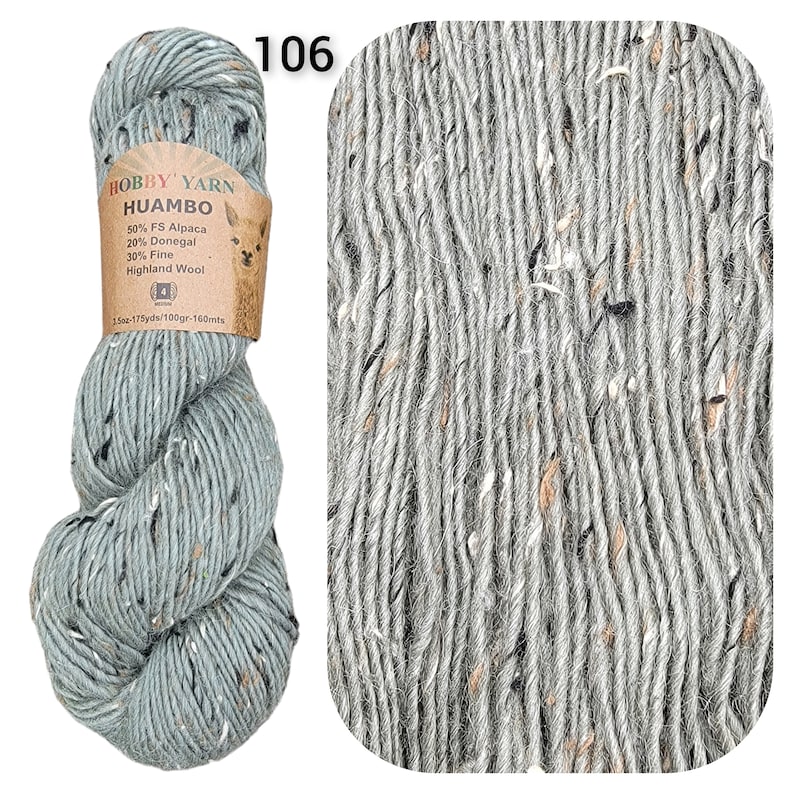 May include: A skein of Hobby Yarn Huambo in color 106. The yarn is a light blue-grey with flecks of black, white, and brown. The label indicates it's 50% FS Alpaca, 20% Donegal, and 30% Fine Highland Wool. The skein weighs 3.5 oz and is 175 yards long.