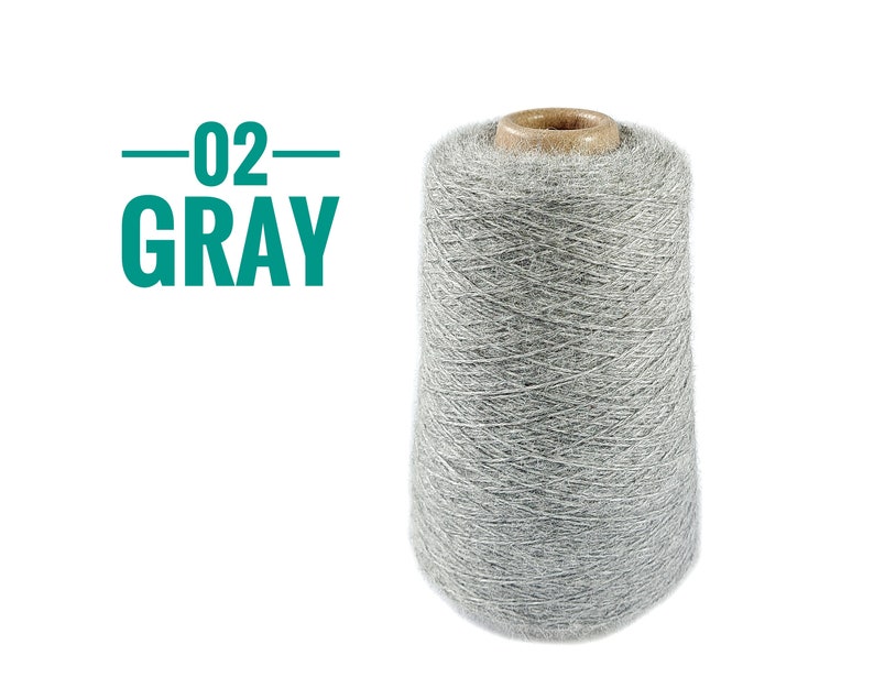 Pode incluir: Um cone grande de fio cinza-claro com uma apar&ecirc;ncia felpuda e texturizada. O topo do cone apresenta um n&uacute;cleo de papel&atilde;o marrom. &Agrave; esquerda do cone de fio, o texto 02 GRAY est&aacute; impresso em uma fonte sem serifa verde-azulado com linhas.
