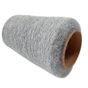 Pode incluir: Um grande cone cil&iacute;ndrico de fio cinza-claro com uma superf&iacute;cie texturizada e felpuda. O fio &eacute; enrolado firmemente em torno de um n&uacute;cleo de papel&atilde;o marrom resistente, exibindo uma apar&ecirc;ncia macia e consistente em toda a bobina.