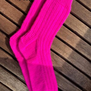 May include: A pair of bright pink ribbed knit socks. The socks are displayed on a wooden surface. The number "7106" is printed in white on the top left corner of the image. The socks are a vibrant, solid color.
