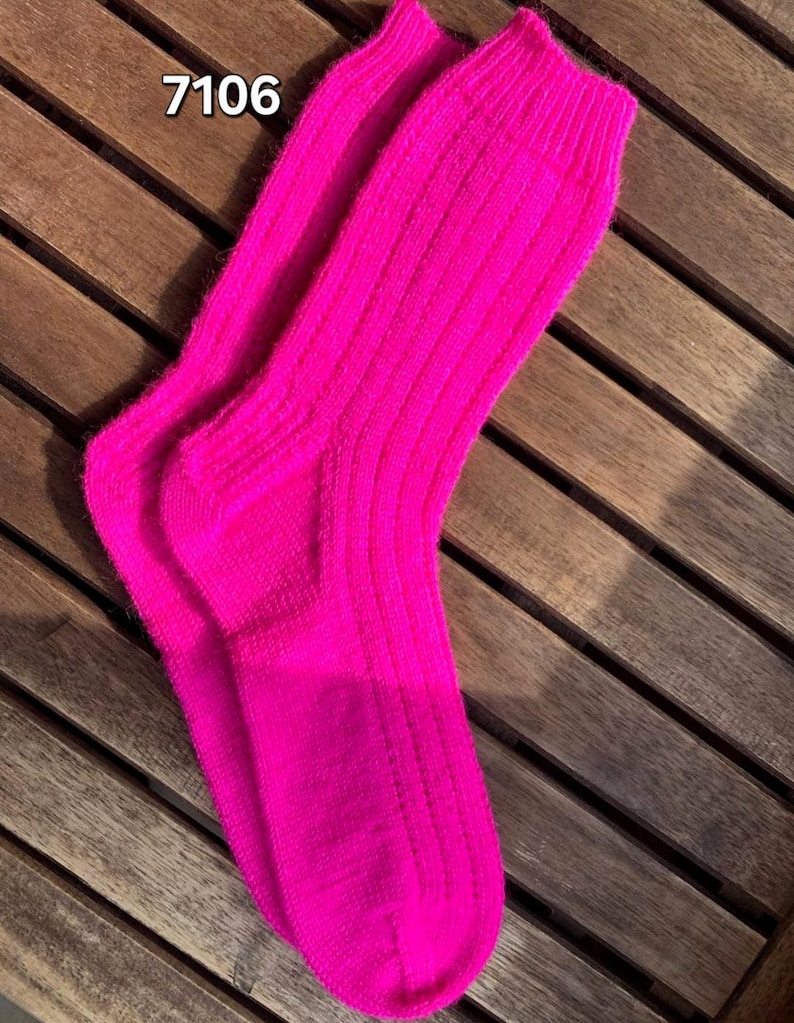 May include: A pair of bright pink ribbed knit socks. The socks are displayed on a wooden surface. The number "7106" is printed in white on the top left corner of the image. The socks are a vibrant, solid color.