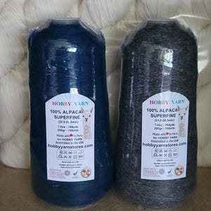 Pode incluir: Dois cones de fio 100% alpaca superfina, um azul escuro e outro cinza carv&atilde;o, embalados em pl&aacute;stico transparente. Os r&oacute;tulos apresentam uma ilustra&ccedil;&atilde;o de alpaca, o texto Hobby Yarn, 7.0oz, 764yds, 200gr, 700mts e instru&ccedil;&otilde;es de cuidado.