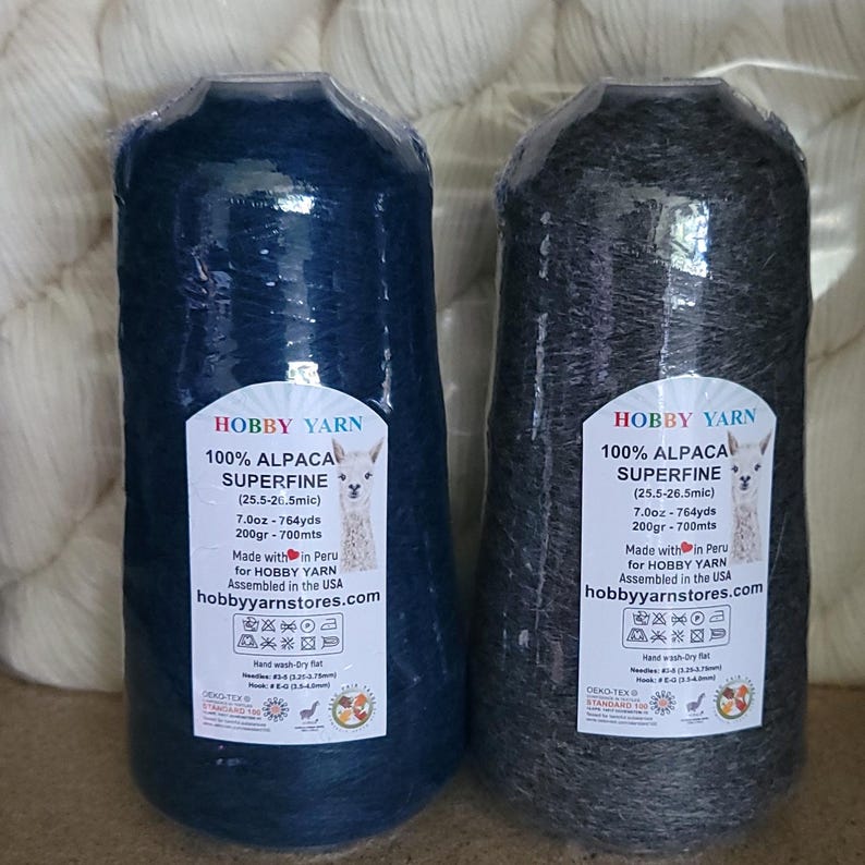 Pode incluir: Dois cones de fio 100% alpaca superfina, um azul escuro e outro cinza carv&atilde;o, embalados em pl&aacute;stico transparente. Os r&oacute;tulos apresentam uma ilustra&ccedil;&atilde;o de alpaca, o texto Hobby Yarn, 7.0oz, 764yds, 200gr, 700mts e instru&ccedil;&otilde;es de cuidado.