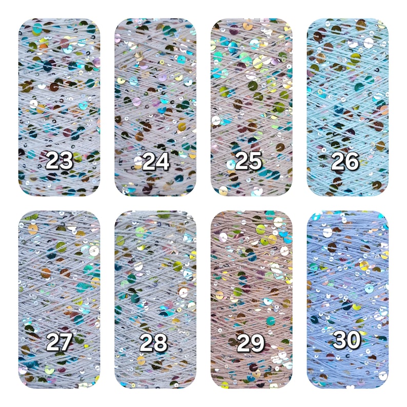 May include: Eight spools of yarn arranged in two rows, labeled 23 through 30. Each spool features light-colored thread interwoven with iridescent, reflective sequins that shimmer in various colors. The spools are rectangular with rounded corners.