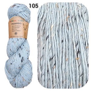May include: A skein of light blue Hobby Yarn Huambo, speckled with dark and light flecks. The label indicates the yarn is made of alpaca, Donegal, and Highland wool. The number "105" is printed in the upper left corner.