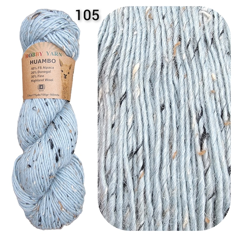 May include: A skein of light blue Hobby Yarn Huambo, speckled with dark and light flecks. The label indicates the yarn is made of alpaca, Donegal, and Highland wool. The number "105" is printed in the upper left corner.
