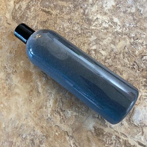 May include: A clear, cylindrical bottle with a black cap. The bottle contains a blue liquid with a gradient effect, transitioning from a darker shade at the top to a lighter shade towards the bottom. The bottle is lying horizontally.