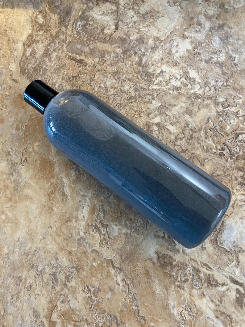 May include: A clear, cylindrical bottle with a black cap. The bottle contains a blue liquid with a gradient effect, transitioning from a darker shade at the top to a lighter shade towards the bottom. The bottle is lying horizontally.