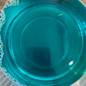 Puede incluir: Un bol de vidrio transparente lleno de un l&iacute;quido azul turquesa brillante. Hay peque&ntilde;as burbujas blancas alrededor del borde del l&iacute;quido.