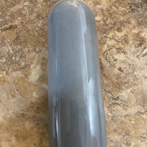 May include: A tall, cylindrical bottle with a black cap. The bottle has a gradient effect, transitioning from a light gray at the top to a darker gray at the bottom. The bottle is made of a clear material.