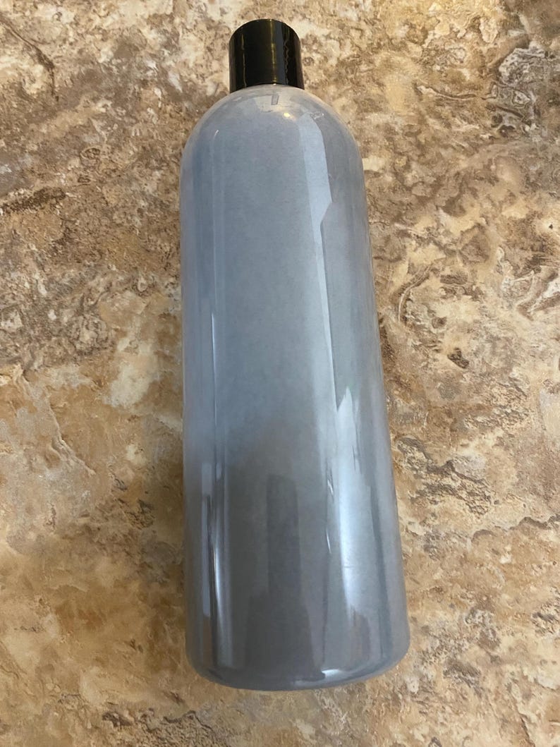 May include: A tall, cylindrical bottle with a black cap. The bottle has a gradient effect, transitioning from a light gray at the top to a darker gray at the bottom. The bottle is made of a clear material.