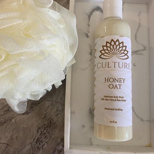 May include: A bottle of Honey Oat body wash with a white label and gold accents, alongside a white loofah and a white marble tray. The label reads "CULTURE NATURAL HANDMADE SPA". The bottle contains 9.5 fl oz of product.