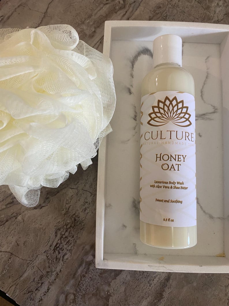 May include: A bottle of Honey Oat body wash with a white label and gold accents, alongside a white loofah and a white marble tray. The label reads "CULTURE NATURAL HANDMADE SPA". The bottle contains 9.5 fl oz of product.