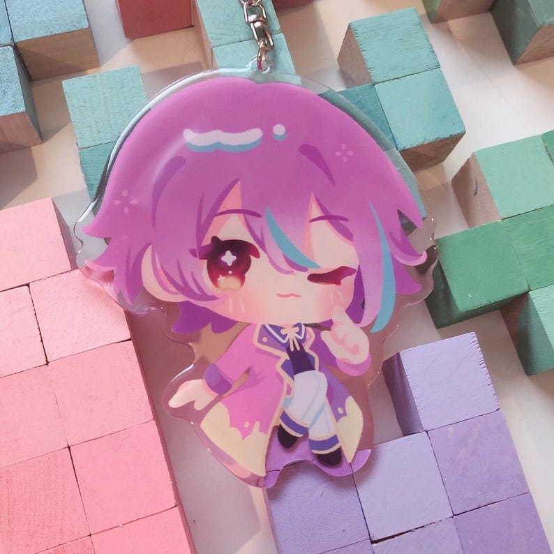 May include: A clear acrylic charm depicting a cartoon character with pink hair, blue highlights, and a pink and purple outfit. The charm has a silver keychain attachment. The character is winking and has a cute expression.