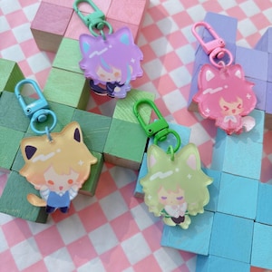May include: Four colorful acrylic keychains featuring anime-style characters with cat ears. Each keychain has a different color scheme: purple, pink, yellow, and green. The keychains have metal clasps for easy attachment.