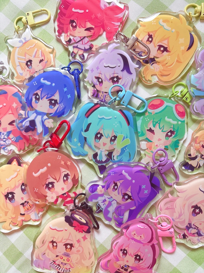 May include: A collection of colorful anime-style acrylic keychains featuring various characters with large eyes and vibrant hair. Each keychain has a different design and is attached to a metal clasp.
