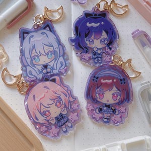 Puede incluir: Cuatro llaveros de personajes de estilo anime con herrajes dorados. Los llaveros presentan personajes con diferentes colores de cabello: blanco, morado, rosa y rojo. Cada personaje est&aacute; rodeado de detalles en forma de estrella y tiene un dise&ntilde;o de orejas de gato o lazo.