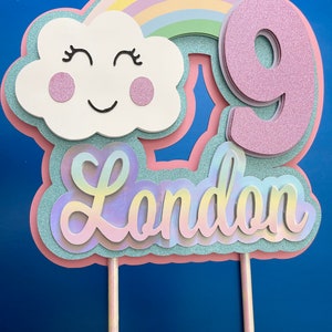May include: A pink and blue cake topper with a rainbow, a cloud with a smiley face, the number 9, and the name "London".