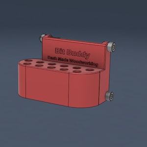 Op de afbeelding: Rode plastic bit houder met 12 slots voor freesbits. De houder heeft de tekst "Bit Buddy Dash Made Woodworking" op de voorkant.