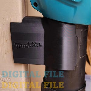 Könnte beinhalten: Eine 3D-gedruckte schwarze Wandhalterung für einen Makita-Laubbläser. Die Halterung ist so konzipiert, dass sie den Gebläse sicher an einer Wand befestigt. Die Halterung hat eine schwarze Oberfläche und das Makita-Logo ist auf der Vorderseite sichtbar.