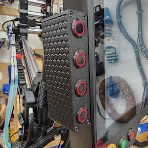 Puede incluir: Un panel de control negro con cuatro botones rojos y un patrón de panal. El panel está montado en una máquina con una pantalla táctil que muestra el texto "MAS950 Spindle Driver, Conc. Vol. 50V/min".