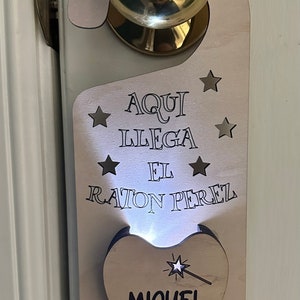 May include: Wooden tooth door hanger with a light-up tooth that says "Miguel" and the text "Aqui Llega El Raton Perez" with stars around the text.