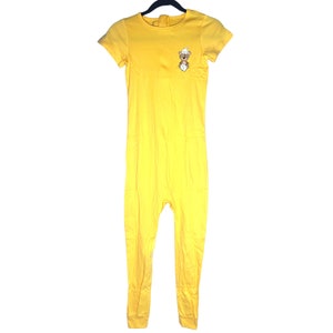 May include: A yellow one-piece jumpsuit with short sleeves and a small embroidered bear on the chest.