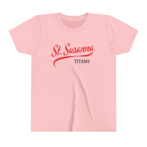 Pode incluir: Camiseta rosa com um gráfico vermelho "St. Susanna Titans".
