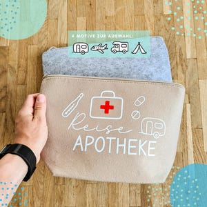 Könnte beinhalten: Zwei Reise-Filztaschen, eine graue und eine beige, mit Reißverschlüssen. Die beige Tasche hat weiße Grafiken eines Erste-Hilfe-Kastens, Pillen, eines Thermometers und eines Wohnmobils mit dem Text "Reise Apotheke". Die graue Tasche hat Illustrationen eines Wohnmobils, Flugzeugs, Wohnwagens und Zeltes.