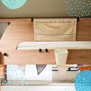 Könnte beinhalten: Ein helles Etagenbett aus Holz mit einem beigefarbenen Stofforganizer und einem kleinen weißen Behälter. Das Bett hat eine weiße Matratze und ist mit einer Girlande aus dreieckigen Flaggen in verschiedenen Farben geschmückt. Der Hintergrund hat ein hellgrünes und blaues Tupfenmuster.