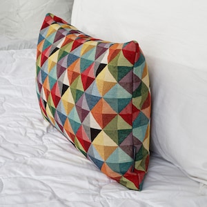 Könnte beinhalten: Ein farbenfrohes geometrisches Musterkissen mit verschiedenen Farben wie Rot, Gelb, Blau, Grün und Lila.