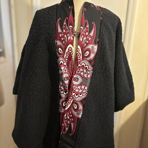 May include: Black fleece cape with a red, white, and black paisley pattern on the front.