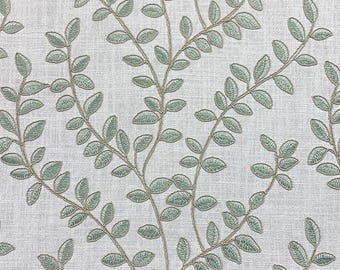 May include: A light gray fabric featuring an embroidered pattern of climbing vines with sage green leaves and thin tan stems. The textile has a visible woven texture, and the embroidery creates a raised, detailed botanical design across the surface.