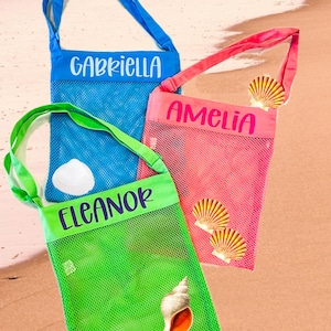 May include: Three mesh beach bags with personalized names. The bags are blue, pink, and green. Each bag has a seashell design.