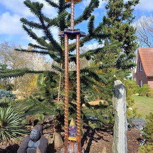 Puede incluir: Una escultura decorativa para exteriores con postes de color cobre y una base morada y dorada. La escultura tiene un diseño escalonado con un cuadrado amarillo en la parte superior. Una estatua de gorila y una figura en forma de cono están en primer plano.
