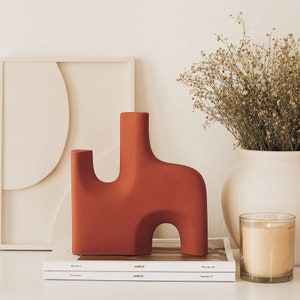 May include: A terracotta-coloured abstract ceramic sculpture with a unique, organic shape. The sculpture is sitting on top of two magazines, one titled "cook/life" and the other titled "cook/life" with the volume number "17".