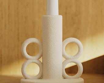 May include: A cream-colored candle holder with a textured surface, holding a white candle. The holder features a cylindrical base with two sets of stacked ring accents. The design is minimalist and modern, suitable for home decor.