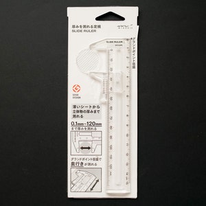May include: A white plastic slide ruler with a caliper attachment. The ruler measures up to 120 mm and the caliper measures up to 60 mm. The packaging says "SLIDE RULER" and "0.1mm-120mm".