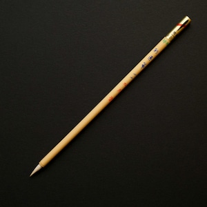 Puede incluir: Un pincel de caligrafía con un mango de madera marrón claro y una punta blanca. El mango tiene texto y diseños coloridos. El extremo del mango es dorado. El pincel está sobre un fondo negro.