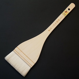 Puede incluir: Un gran pincel de caligrafía japonesa plano de madera, con un mango largo y un cabezal ancho y rectangular. El pincel tiene un acabado de madera natural y cerdas blancas. Texto impreso en el mango.