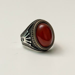 May include: A silver ring featuring a red carnelian stone set within a crown design.