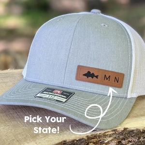 May include: Gray and white trucker hat with a brown leather patch featuring a fish silhouette and the letters "MN".