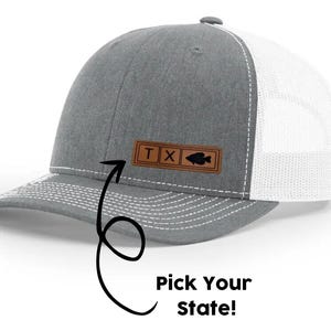 May include: Gray and white trucker hat with a brown leather patch that says "TX" and has a silhouette of a fish.  Pick Your State!