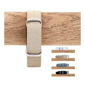 Op de afbeelding: Een beige nylon horlogeband met een geweven textuur en zilverkleurige metalen hardware. De band is voorzien van een rechthoekige gesp en twee schuifbare lusjes. Andere getoonde kleuren zijn wit, lichtbruin, blauw en zwart.