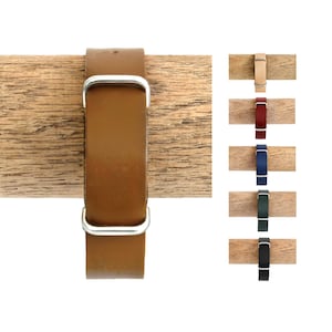 May include: A collection of leather watch straps featuring a smooth finish and silver-toned metal buckles. The straps are displayed in various colors including tan, red, blue, dark green, and black, each wrapped around a wooden cylindrical holder.