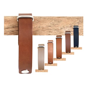 May include: A collection of six leather bracelets in varying shades of brown, tan, and navy blue. Each bracelet features a smooth leather strap, a silver-toned metal buckle, and a single silver-toned metal snap button closure at the bottom end.